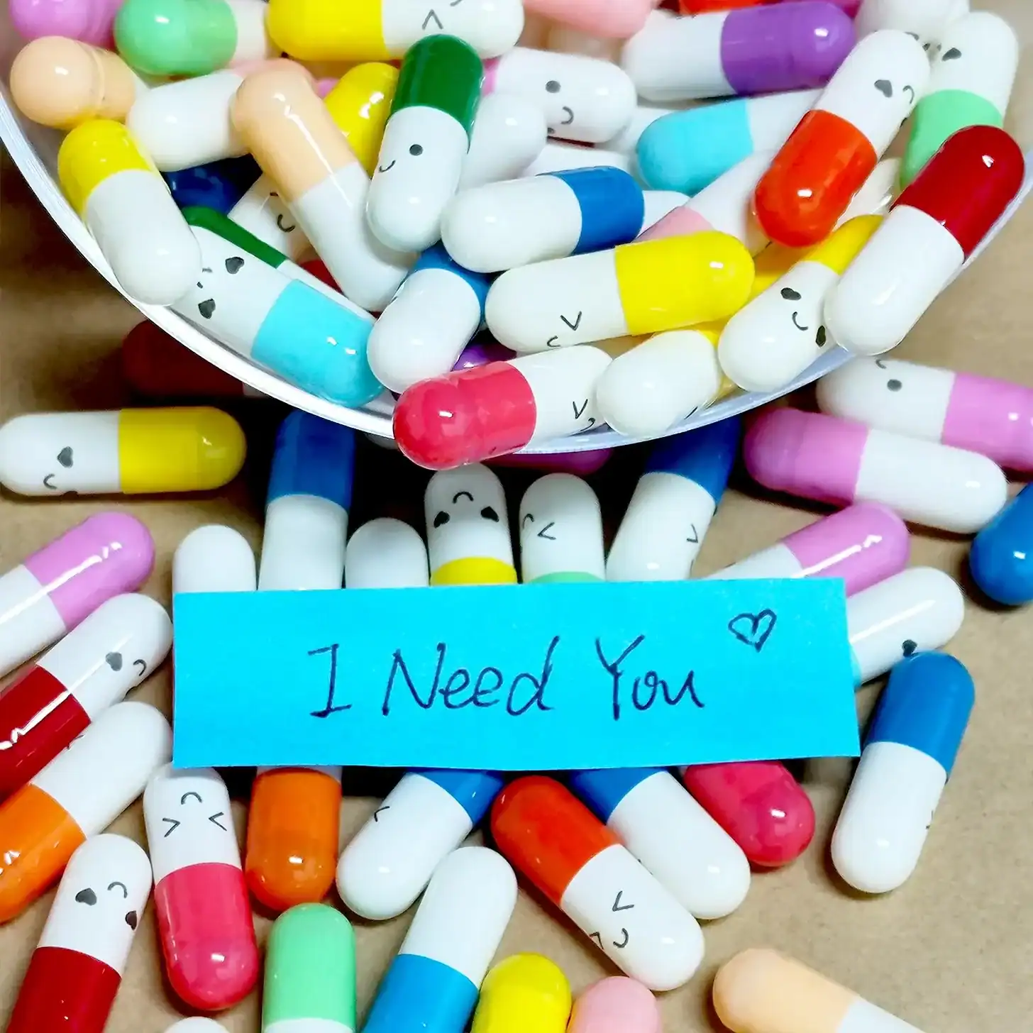Colorful capsules with a note saying "I Need You" surrounded by pills.