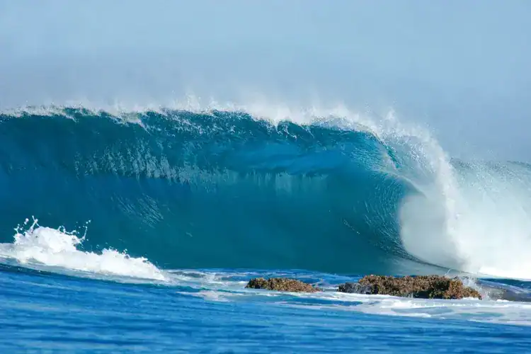 Powerful ocean wave crashing over rocks with spray and foam.