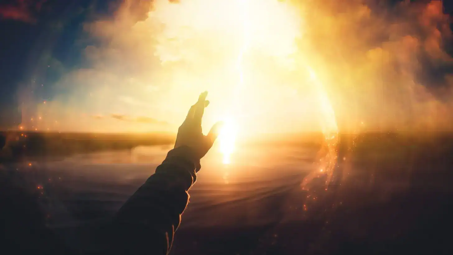 A hand reaching towards a bright, glowing sun in a dramatic sky.